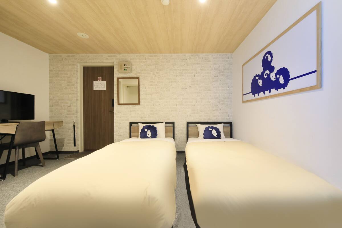 A hotel room with two single beds, a desk with a chair, a television, and a mirror on the wall.