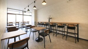 En moderne café med flere borde og stole, store vinduer og hængende lamper.