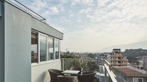 Een balkon met rieten meubilair en uitzicht op een stadsbeeld en bergen.