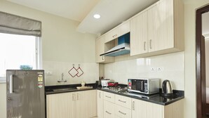 Een compacte keuken met lichte houten kastjes, een zwart aanrecht, een roestvrijstalen koelkast, een magnetron, een waterkoker en een broodrooster.