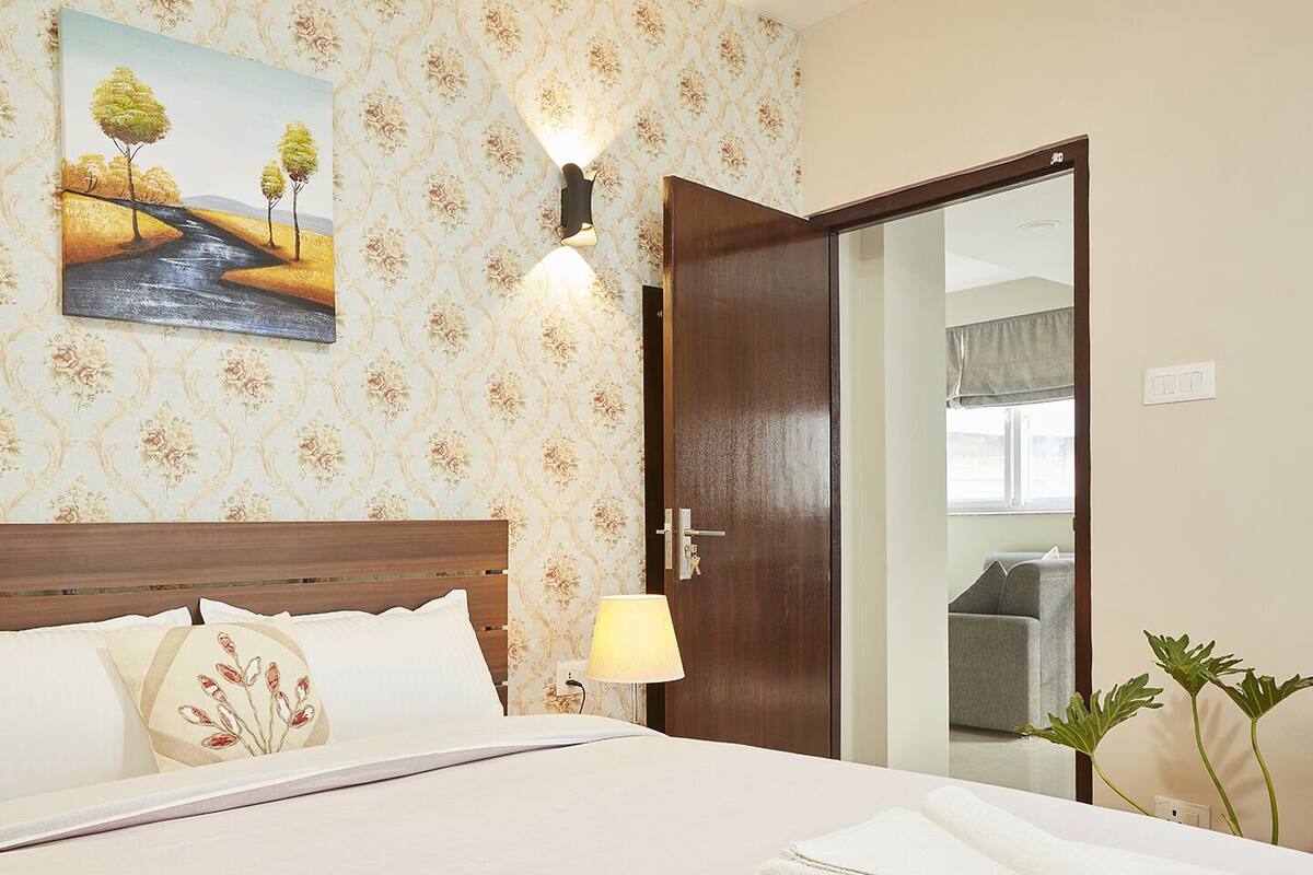 Ein Hotelzimmer mit Bett, einem Landschaftsbild, einem hölzernen Kopfteil und einer Tür zu einem Balkon.