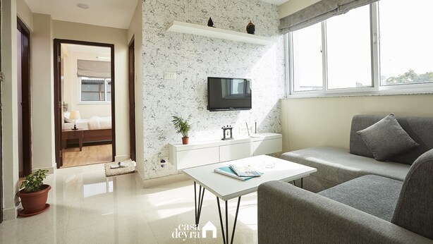 Een moderne woonkamer met een flatscreen televisie, een bank, een bijzettafeltje en een potplant.