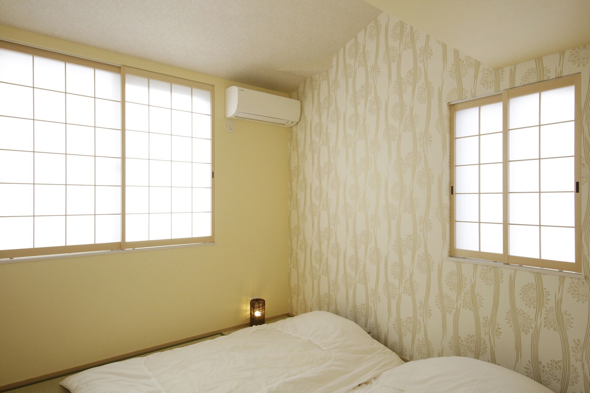Une pièce avec deux fenêtres, un lit et un appareil de climatisation fixé au mur.