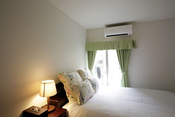 A hotel room with a bed, a bedside lamp, a telephone, and an air conditioning unit.