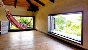 Um quarto espaçoso com piso de madeira, janelas grandes e uma rede.
