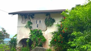 Um edifício com fachada rústica, coberto por vegetação, e uma pequena entrada em arco.