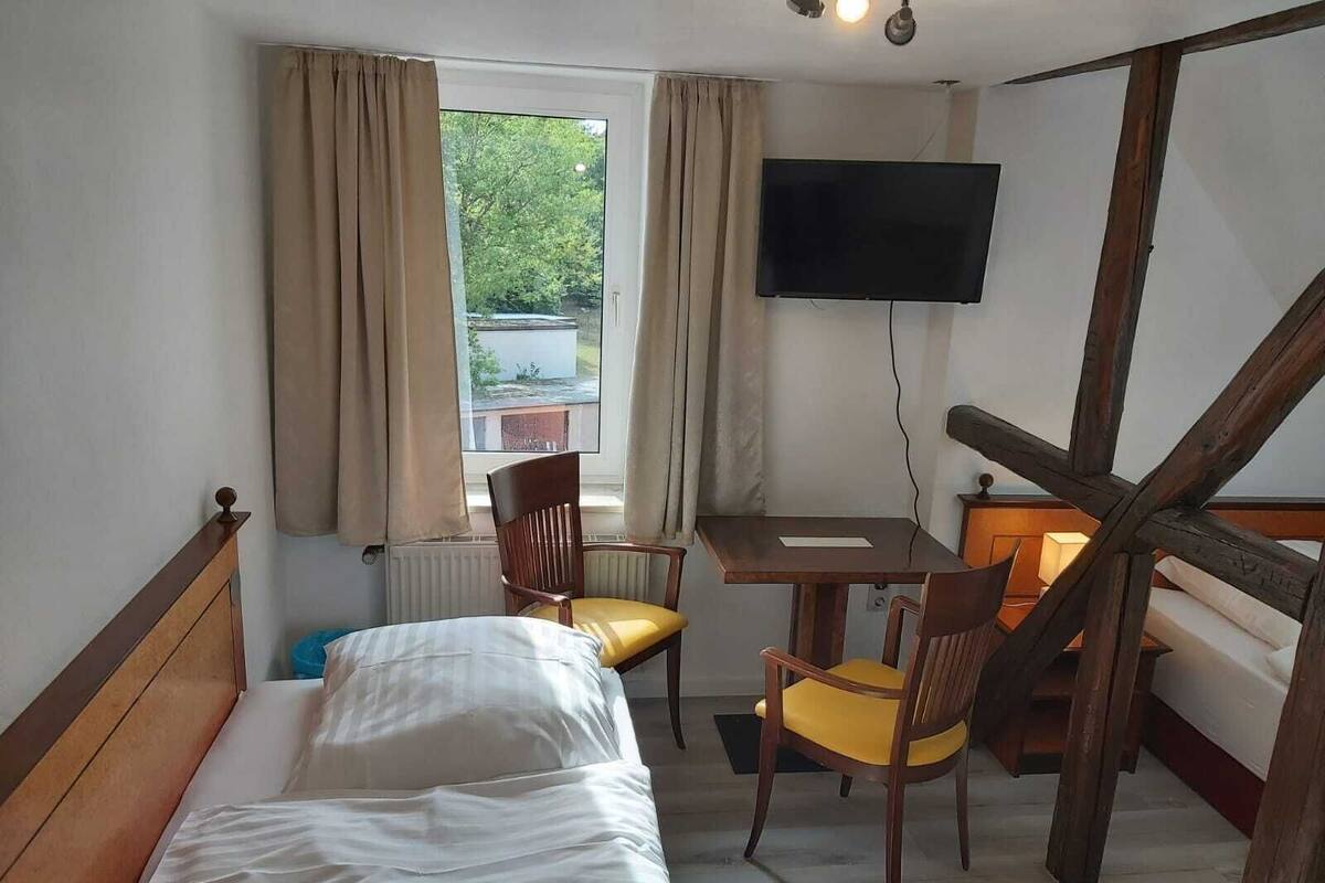 Ein Hotelzimmer mit Bett, Schreibtisch, zwei Stühlen, Fernseher und einem Fenster mit Vorhängen.