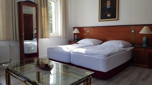 Een hotelkamer met een tweepersoonsbed, een glazen tafel, een houten hoofdbord, een nachtkastje met een lamp, een spiegel en een raam met gordijnen.