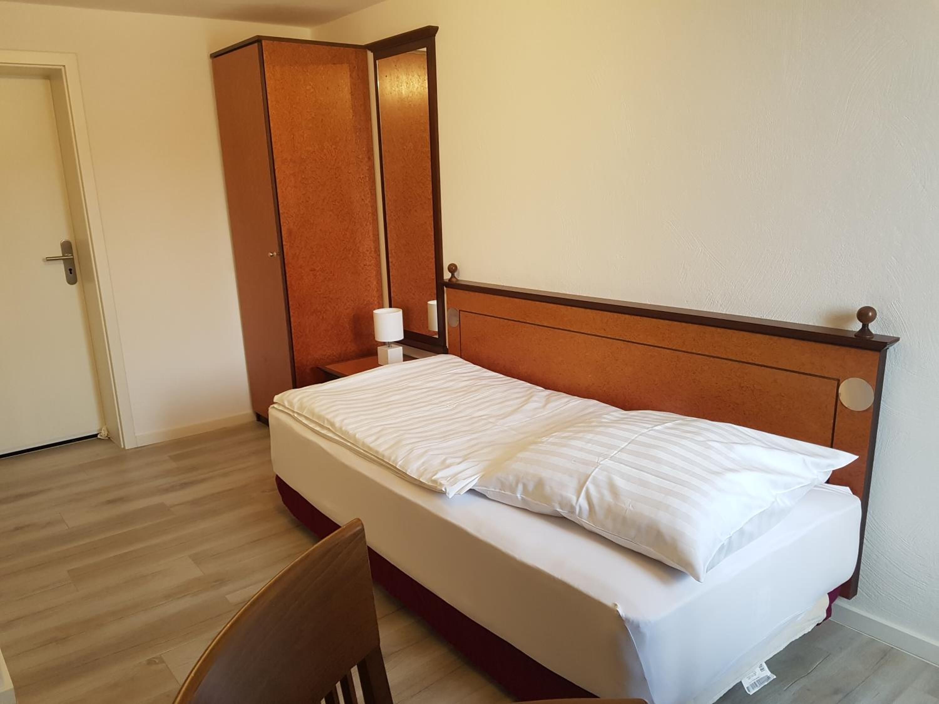 A bedroom with a wooden bed, a nightstand, a mirror, and a wardrobe.