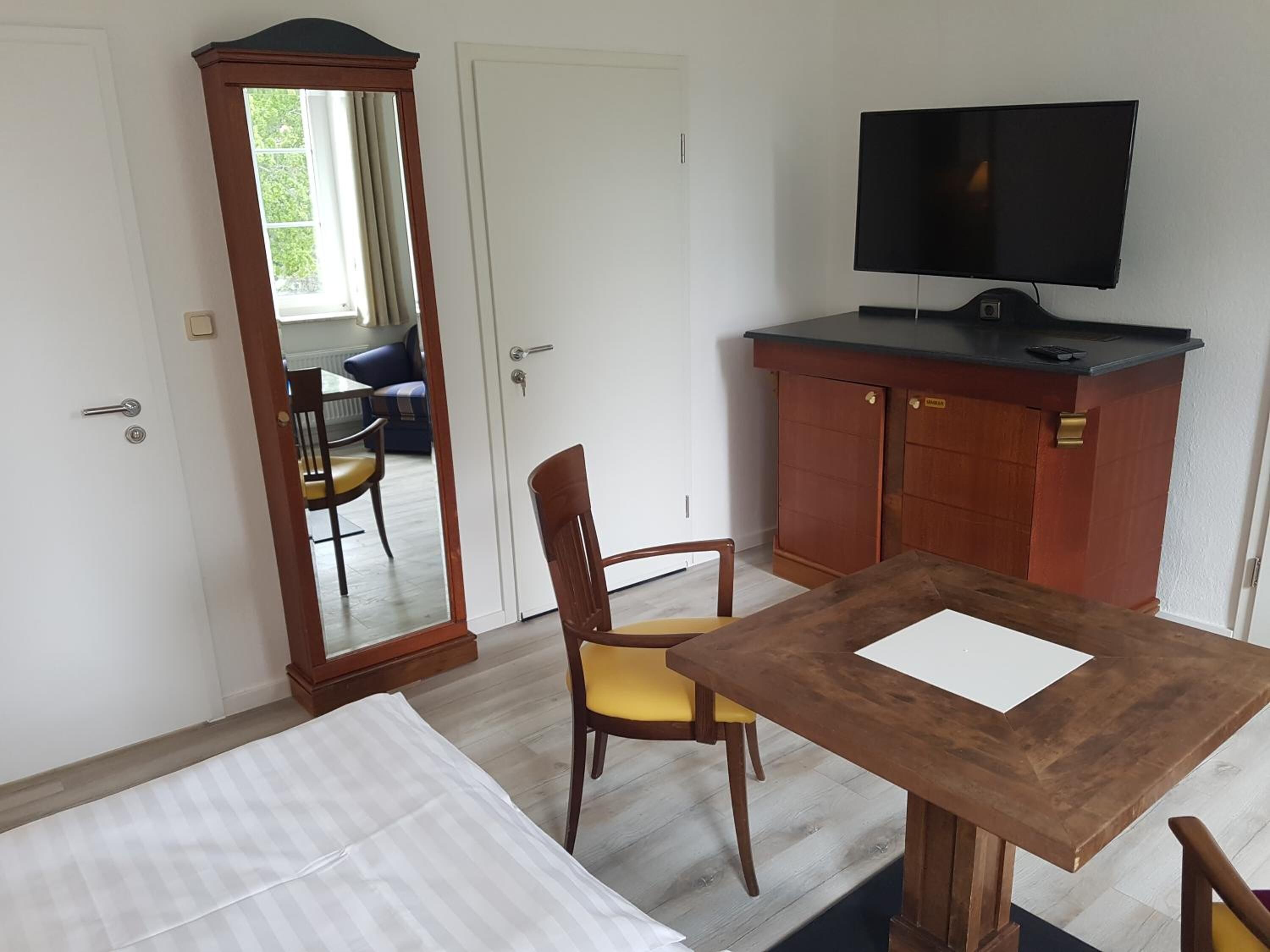 Ein Zimmer mit einem Bett, einem Holztisch, einem Fernseher und einem Kleiderschrank.