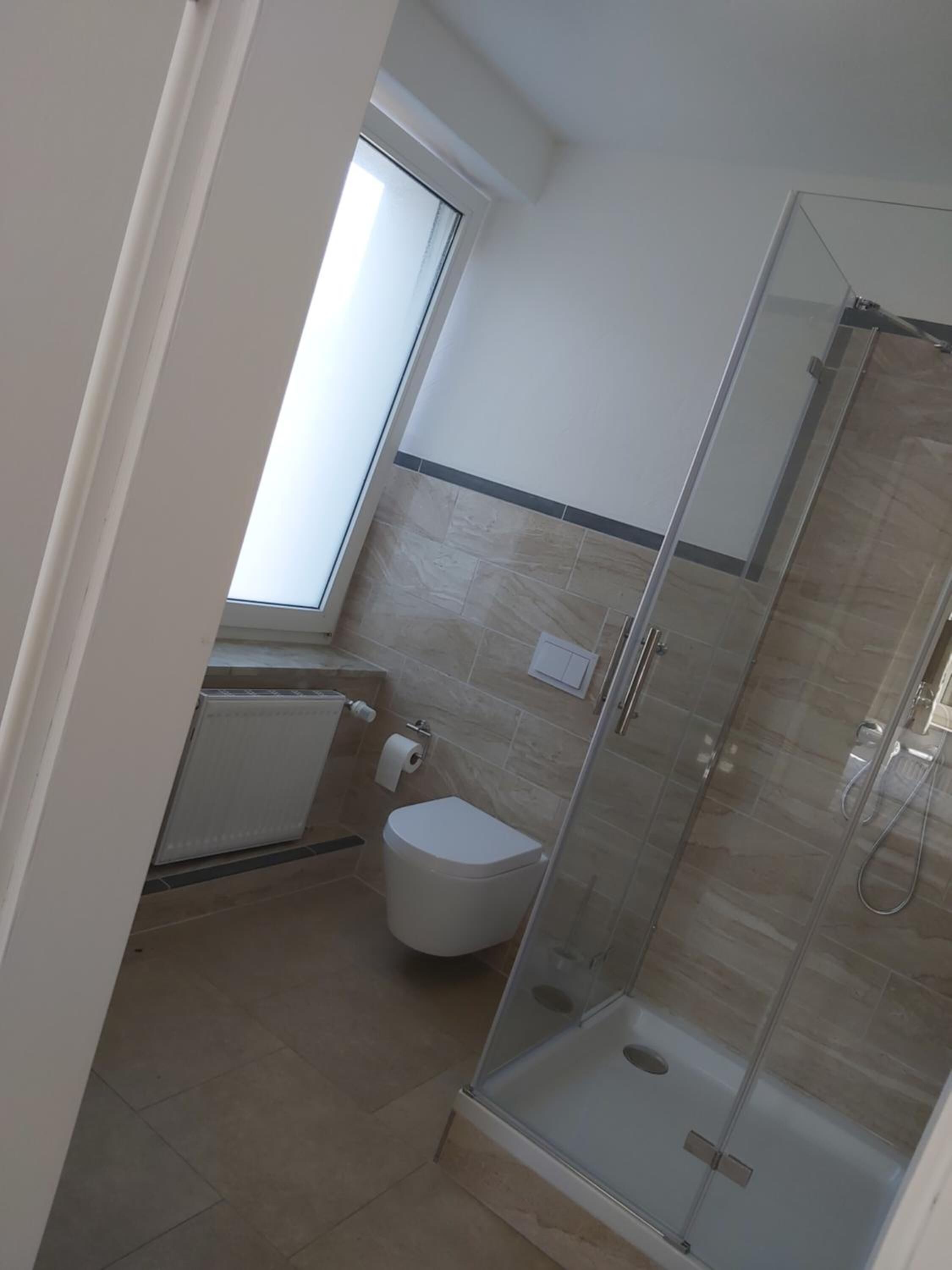 A compact bathroom with a glass-enclosed shower, a toilet, and a window providing natural light.