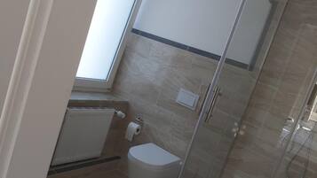 A compact bathroom with a glass-enclosed shower, a toilet, and a window providing natural light.