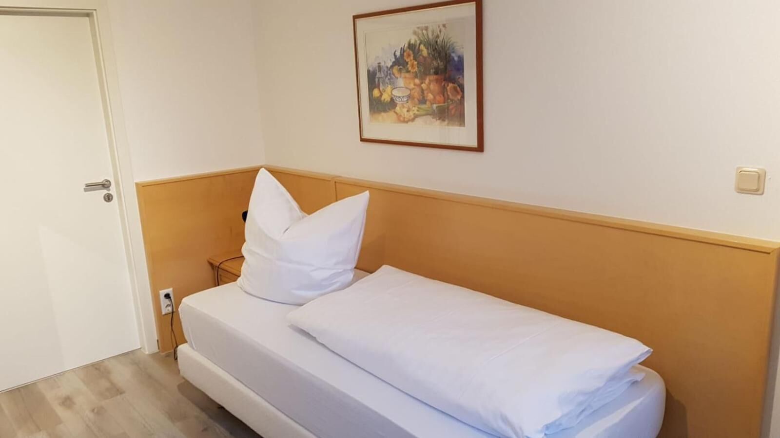 A single bed with white bedding in a room with a wooden headboard and a door on the left.