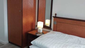 Habitación de hotel con cama, armario, mesita de noche con lámpara y espejo.