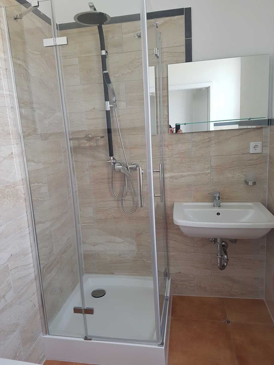 A modern bathroom with a glass-enclosed shower, a white sink, and a mirror above the sink.