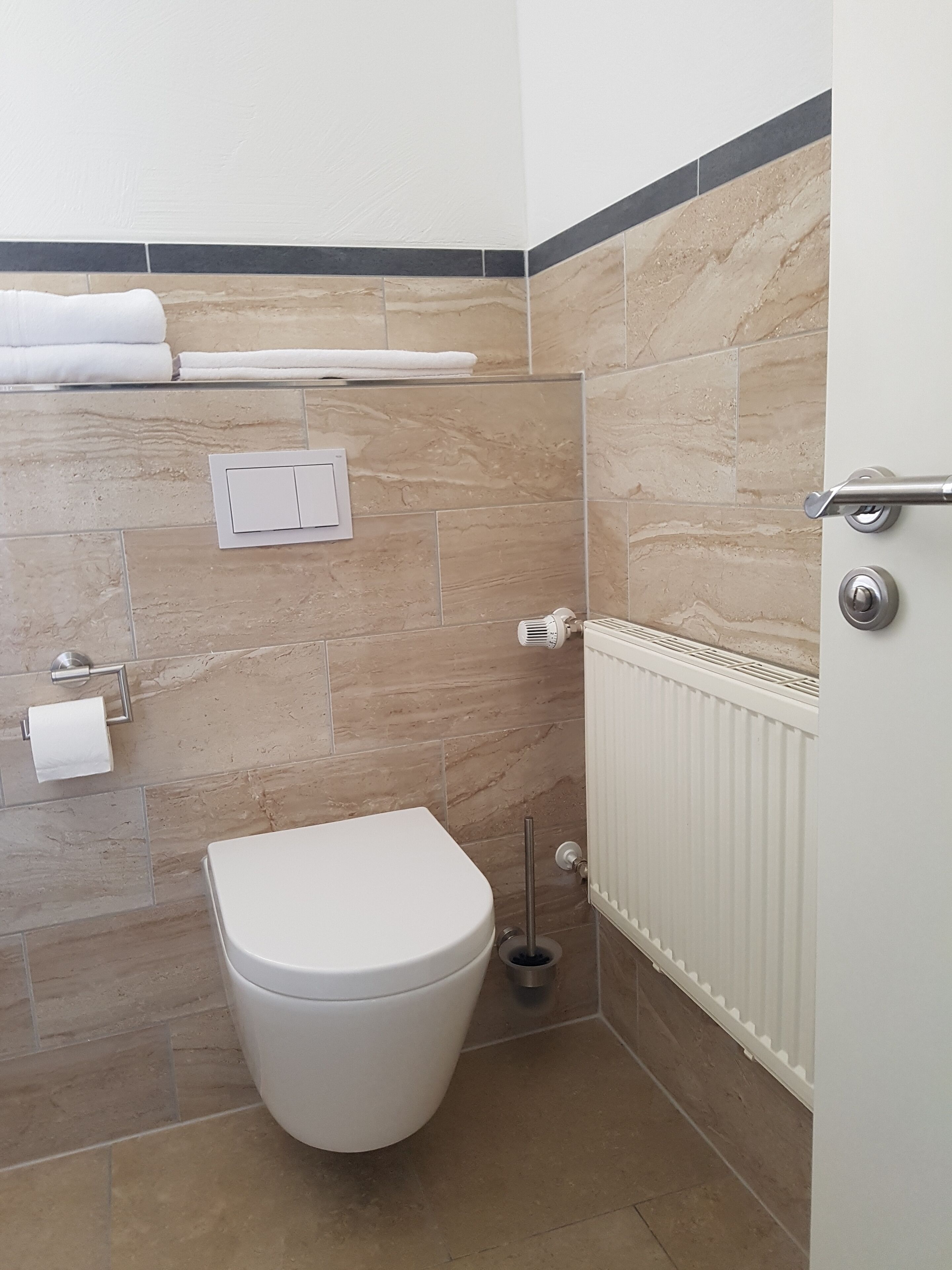 Une salle de bain comprenant des toilettes, un porte-serviettes, un radiateur et un interrupteur fixé au mur.