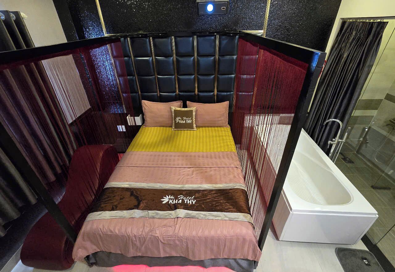 Habitación de hotel con cama, cabecero, mesita de noche y bañera.