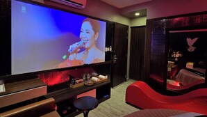 A hotel room with a large flat-screen TV, a red sofa, a small table, and a decorative wall with a bird sculpture. - Kha Thy Hotel (Ho Chi Minh City)