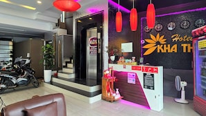 A hotel reception area with a modern design, including a reception desk, a seating area with a brown leather chair, and a motorcycle parked in the background. - Kha Thy Hotel (Ho Chi Minh City)