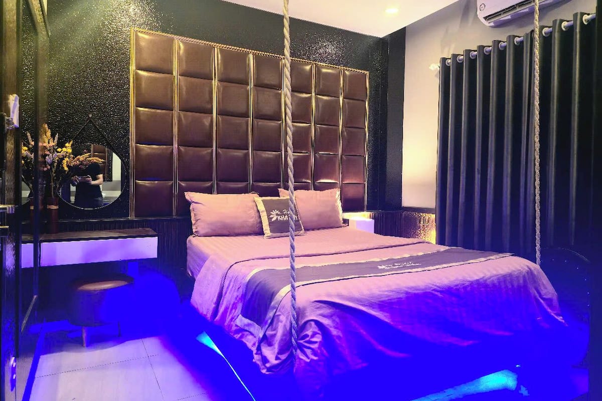 Un dormitorio moderno con cabecera capitonada, una silla colgante y un espejo grande.