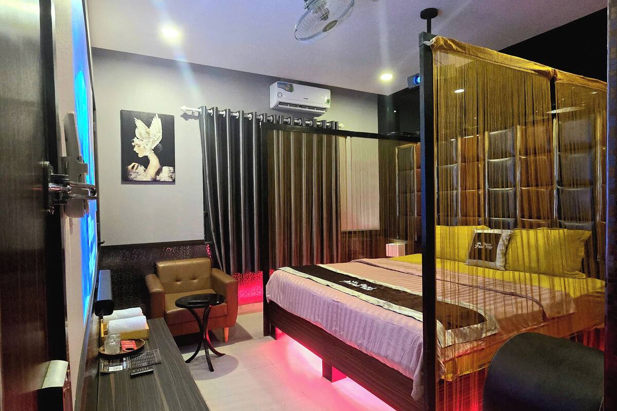 Una habitación de hotel moderna con una cama, un escritorio y una silla. Hay un equipo de aire acondicionado en la pared y un ventilador de techo.
