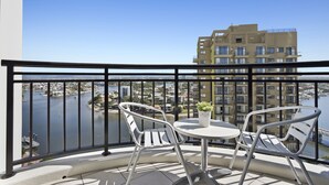 A balcony with two white chairs and a small table, overlooking a body of water and a cityscape.
