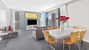 A modern hotel room with a dining area, sofa set, and a flat-screen TV.