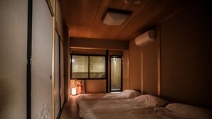 A narrow, dimly lit room with two beds and a small window. - Kyomachiya KINKA (Kyoto)