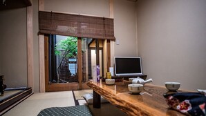 A traditional Japanese room with tatami flooring, a low wooden desk, a television, and a view of greenery outside. - Kyomachiya KINKA (Kyoto)