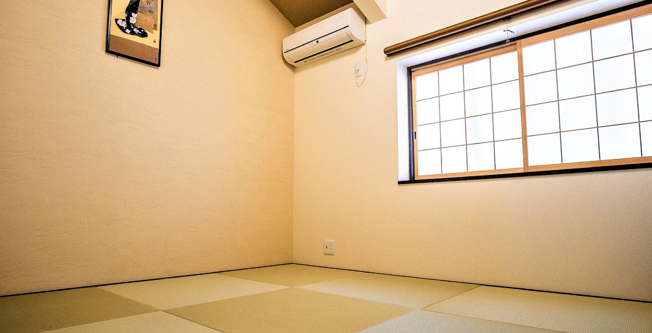 Ein Zimmer mit Tatami-Boden, einem Schieberahmenfenster und einer Wand-Klimaanlage.