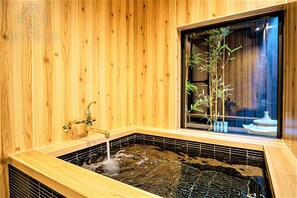 Puisesti sisustettu tila, jossa on kuuma lähde -allas, ikkunalaudalla kasveja ja perinteinen japanilainen estetiikka.