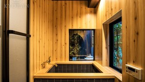 A wooden interior with a built-in hot tub, a window with a view of greenery, and a wall-mounted control panel. - Kyorana Kyogetsutei (Kyoto)
