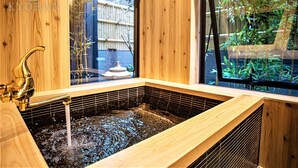 A wooden spa tub with a faucet, a window with a view of bamboo outside, and a tiled floor. - Kyorana Kyogetsutei (Kyoto)