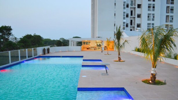 Une piscine dotée d’une terrasse carrelée, entourée de palmiers et avec un bâtiment visible au loin.