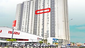 Un grand immeuble à étages, une zone commerciale avec un bâtiment blanc portant l’inscription « ISUZU » et une enseigne « MAKO ».