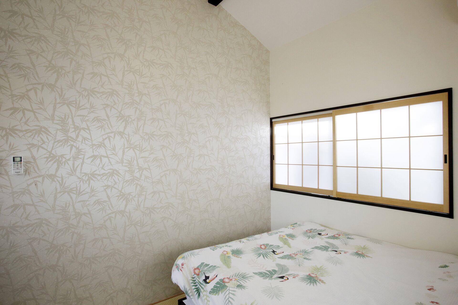 Una habitación pequeña con papel tapiz estampado con bambú, una ventana con pantalla shoji y una cama con edredón floral.