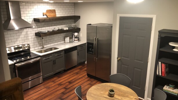 A modern kitchen with stainless steel appliances, a wooden dining table, and a built-in bookshelf.