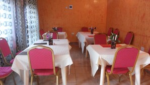 Un espace repas avec des tables et des chaises, un thermostat fixé au mur et des rideaux à motifs.