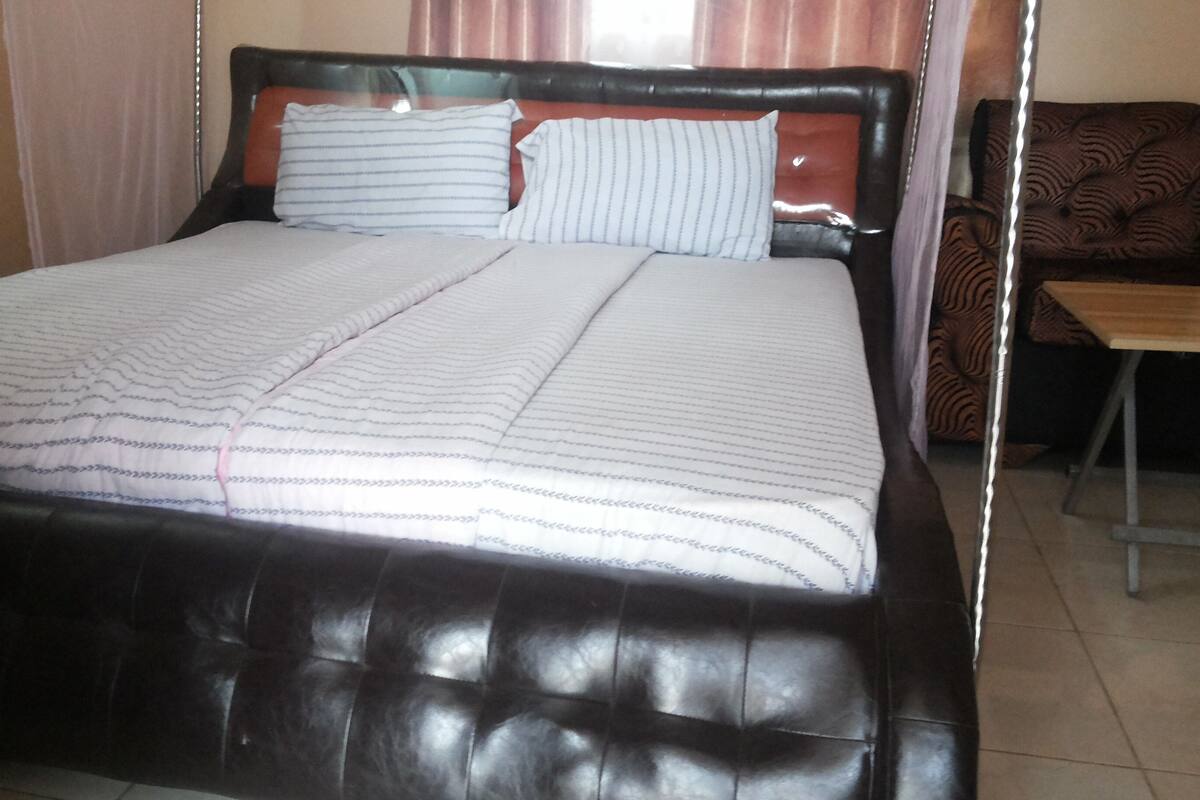 A bed with a dark headboard and white bedding, a wooden nightstand, and a patterned armchair.
