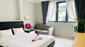 Een hotelkamer met een bed, een grijze bank, een kleine tafel met een plant en een raam met gordijnen.