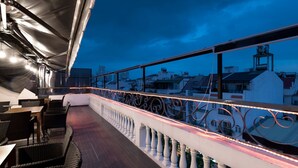 Een terras op het dak met buitenmeubilair en een balustrade met decoratieve verlichting.