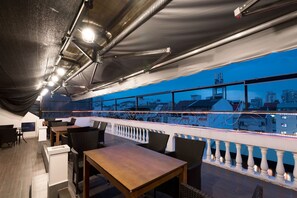 A rooftop bar with a view of the city skyline, featuring tables and chairs, a railing, and a covered area with a metal roof. - New Milano Hotel & Apartment (Ho Chi Minh City)
