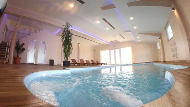 An indoor swimming pool with a wooden floor, surrounded by lounge chairs and a staircase.