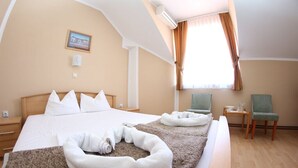 A hotel room with a large bed, two chairs, a small table, and a window with curtains.