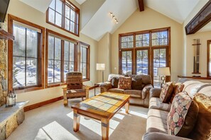 Relax in a spacious living room with a high ceiling and large windows offering a view of the surrounding landscape.