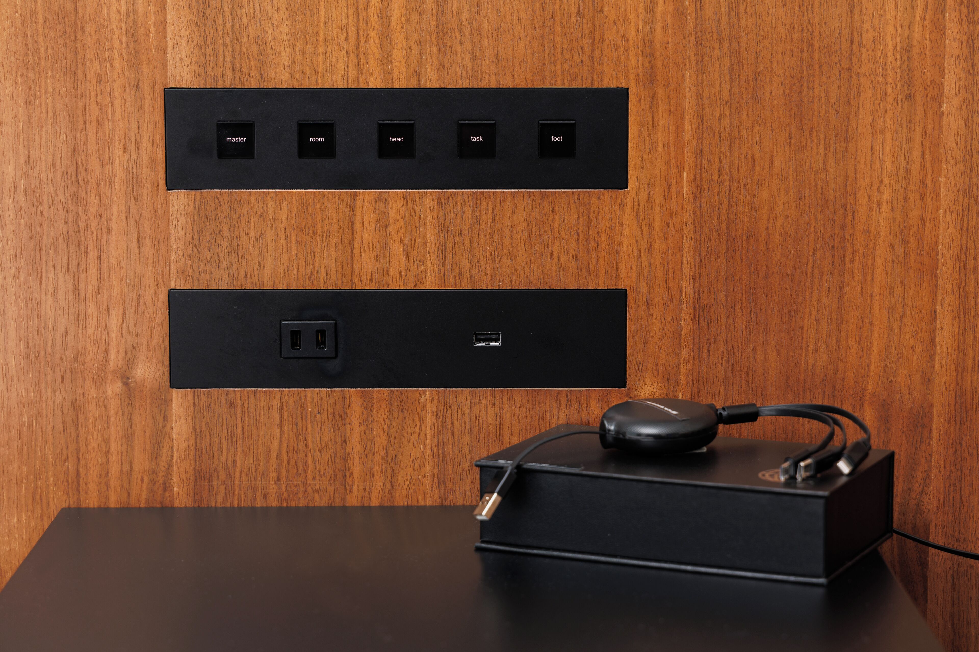 A black charging station with a USB port and a power outlet on a wooden wall.