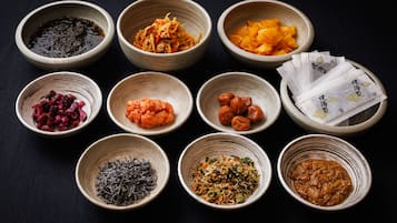 Nine bowls of various food items arranged on a dark surface.