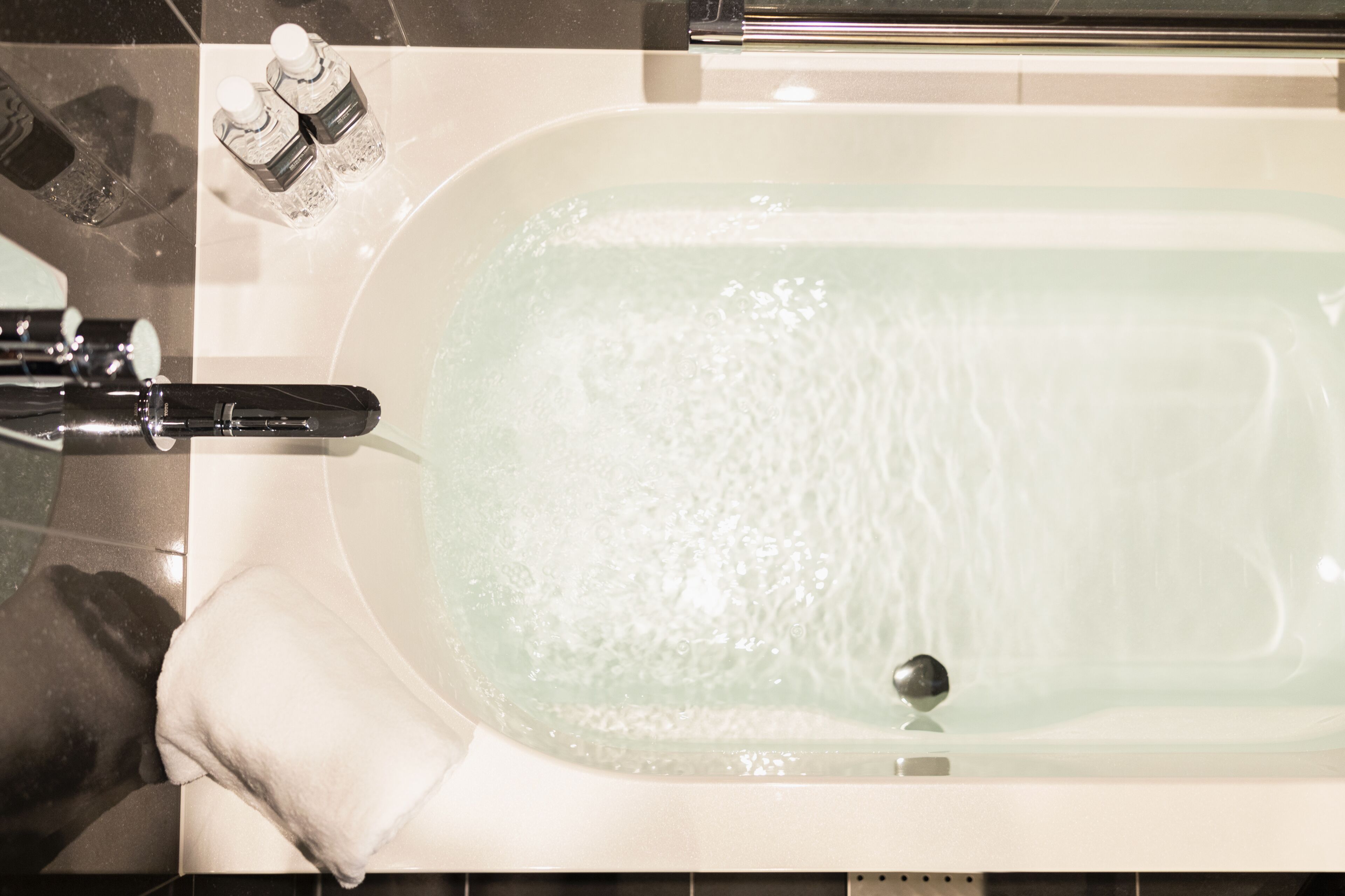 A bathtub with running water, a faucet, and two bottles of bath salts on the edge.
