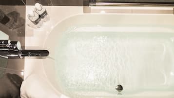 A bathtub with running water, a faucet, and two bottles of bath salts on the edge.