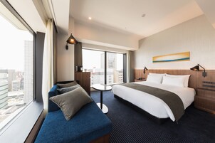 Habitación de hotel con una cama grande, un sofá, una mesita y vistas a la ciudad desde la ventana.